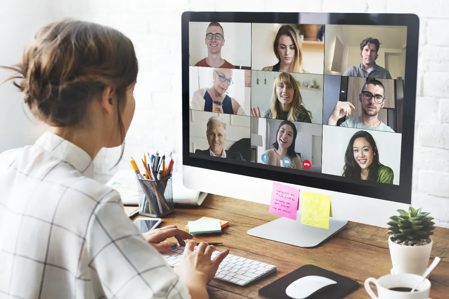 Frau bei Videokonferenz am Arbeitsplatz mit neun Teilnehmern auf dem Bildschirm, professionelle Online-Meeting-Situation